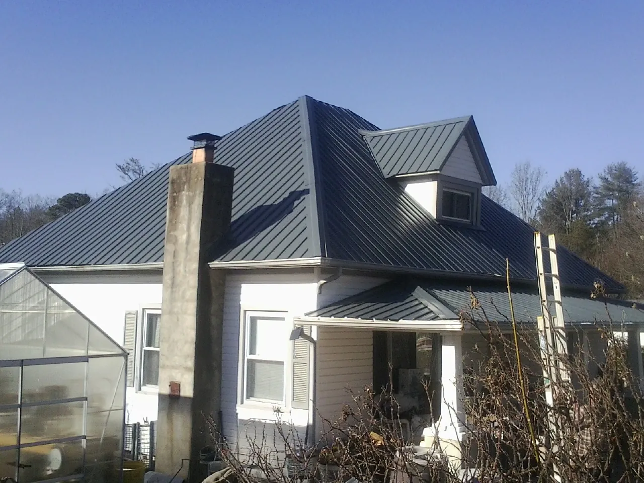 Dark blue standing seam metal roof on a white farmhouse with dormer — Slate & Tile Roof Repair by Roofing Brothers in Carson