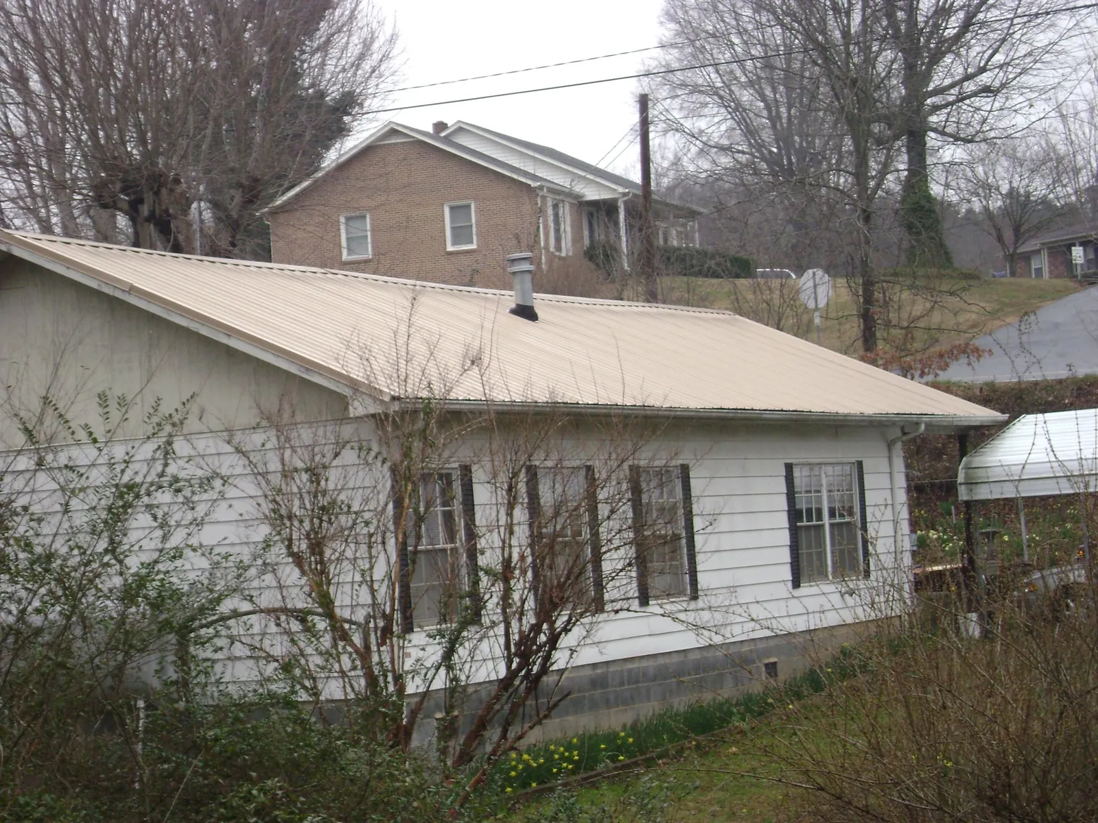 Tan metal roof on a white sided house set into a hillside — Commercial Roofing by Roofing Brothers in Carson